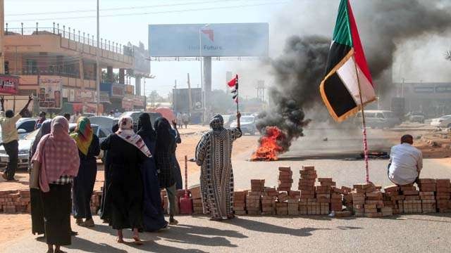Pengunjuk rasa Sudan mengangkat bendera nasional di sebelah penghalang jalan bata di Khartoum hari Senin, sebagai protes terhadap kudeta yang dilakukan militer.(Foto: AFP/Al Jazeera
