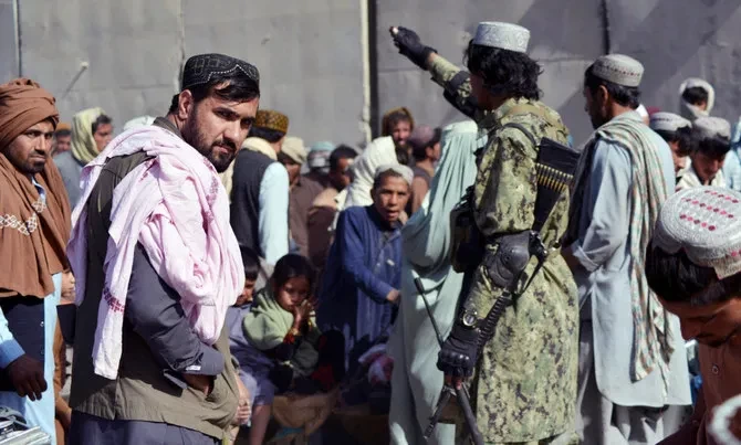 Pejuang Taliban (kanan) memberi isyarat kepada orang-orang yang menunggu untuk menyeberang ke Pakistan di titik penyeberangan perbatasan Afghanistan-Pakistan di Spin Boldak pada 3 November 2021. (Foto: AFP)