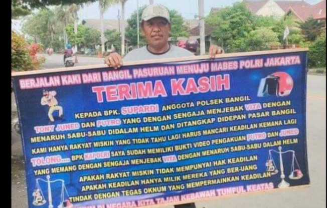 Foto seorang laki-laki Pasuruan membawa banner disebut viral di media sosial. Di dalamnya tertulis jika anggota Polsek Bangil merekayasa kasus. (Foto: ist)