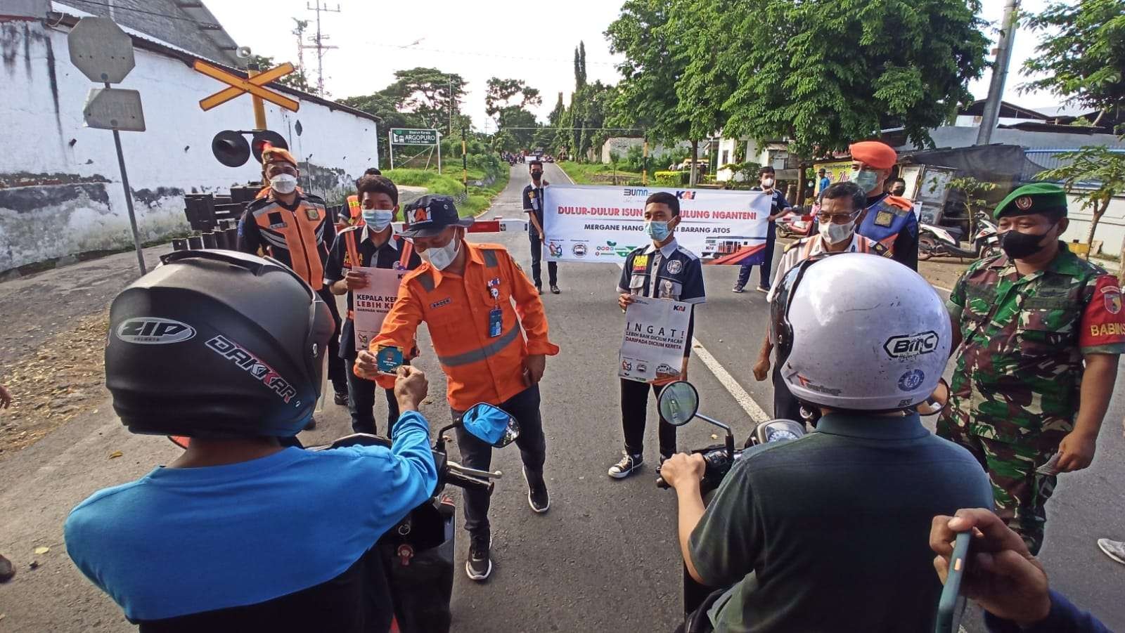 Petugas KAI membagikan stiker kepada pengguna jalan saat melakukan sosialisasi keselamatan di Perlintasan KA sebidang. (Foto: Muh Hujaini/Ngopibareng.id)