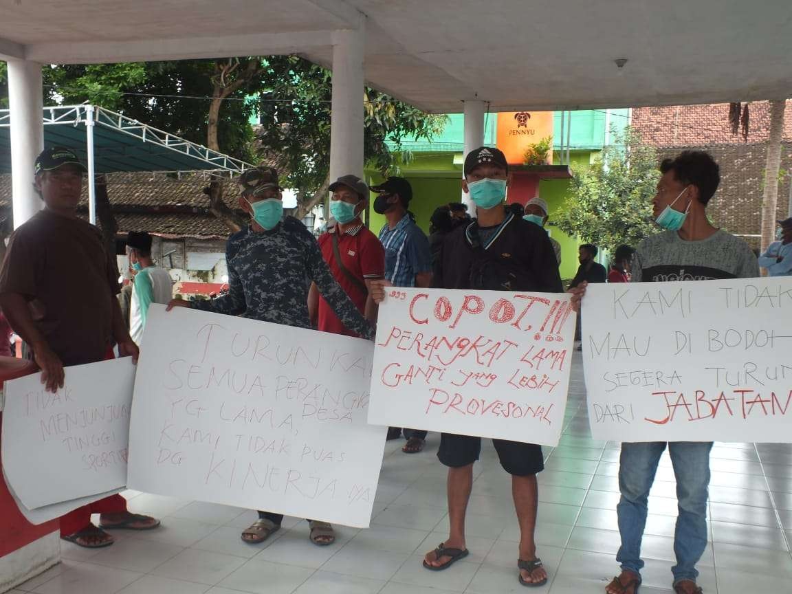 Massa membentangkan poster berisi sejumlah tuntutan kepada Kepala Desa Bangsalsari, Jember (Foto: Rusdi/Ngopibareng.id)