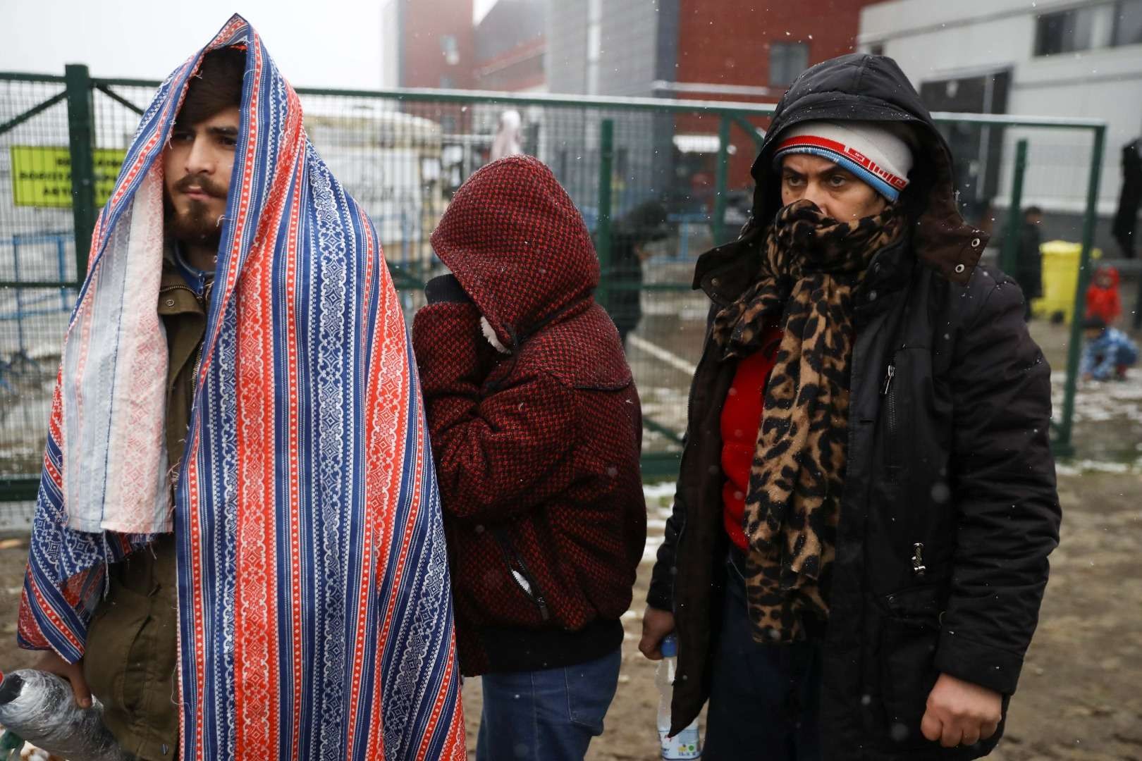 Sejumlah imigran menutupi kepala mereka saat hujan salju di pusat transportasi dan logistik Brudzgi di perbatasan Belarusia-Polandia, di wilayah Grodno, Belarus, Sabtu 27 November 2021. (Foto: reuters)