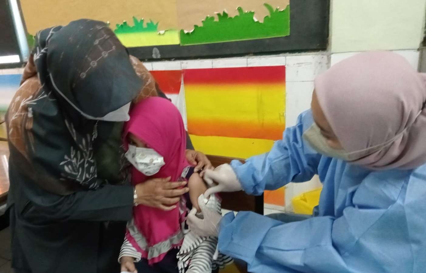 Siswi TK Al Azhar 5 Kemandoran  sedang divaksin covid-19 vaksin is didampingi kepala Sekolah Musani. (Foto: Asmanu Sudarso/ngopibareng.id)