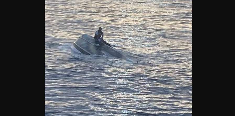 Seorang pria, yang mengatakan dia salah satu dari 40 orang yang meninggalkan Bimini, Bahama, pada hari Sabtu sebelum menghadapi cuaca buruk, duduk di atas kapal yang terbalik di lepas pantai Fort Pierce Inlet, Florida, AS. (Foto: dirilis Penjaga Pantai AS pada 25 Januari 2022, Reuters)