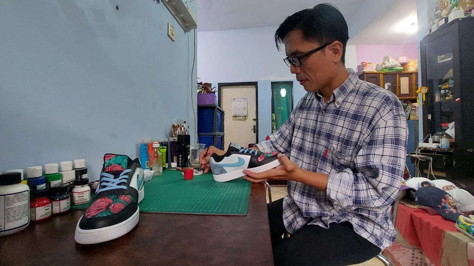 Rinto, warga Perumahan Pondok Gabriela, Kota Probolinggo sedang melukis sepatu pesanan pelanggannya. (Foto: Ikhsan Mahmudi/Ngopibareng.id)