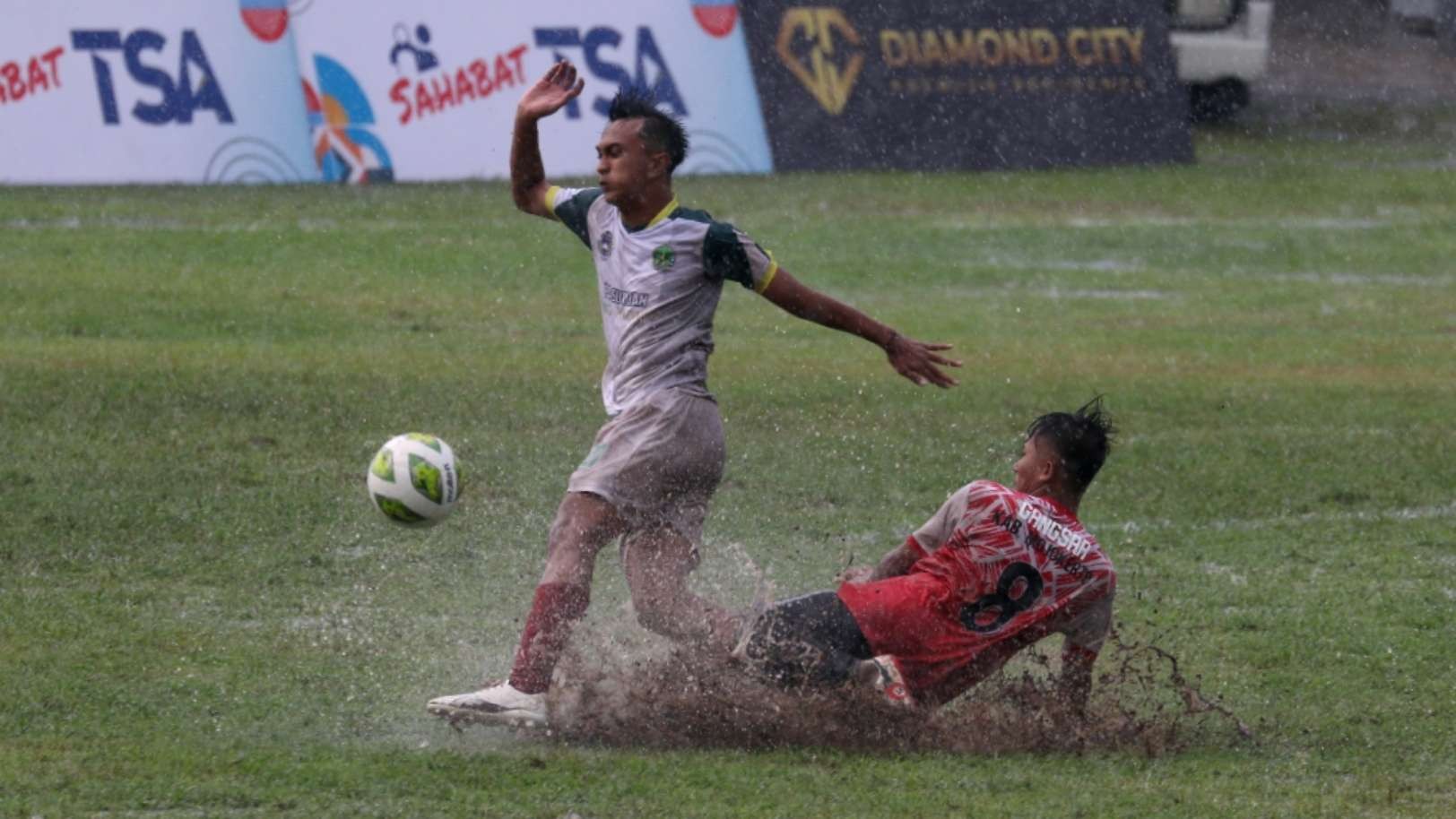 Pemain Kota Pasuruan (putih) saat berebut bola dengan Pemain Mojokerto di tengah genangan air di Stadion Notohadinegoro, Jember. (Foto: Fariz Yarbo/Ngopibareng.id)