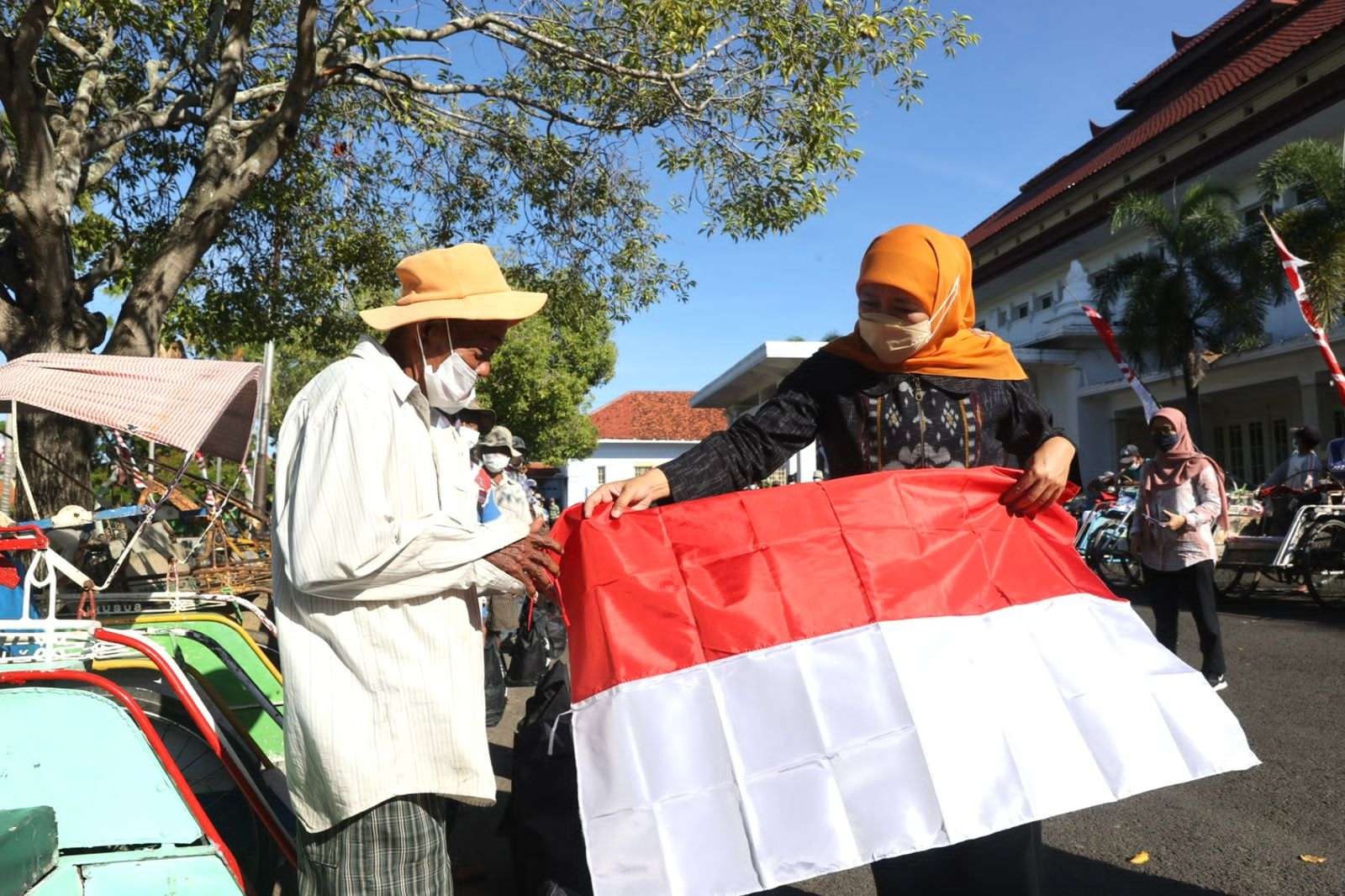 Gubernur Jawa Timur, Khofifah Indar Parawansa (kanan) saat memberikan bendera merah putih kepada tukang becak di Kantor Bakorwil Pamekasan, Sabtu 6 Agustus 2022. (Foto: Dokumentasi Humas Pemprov Jatim)