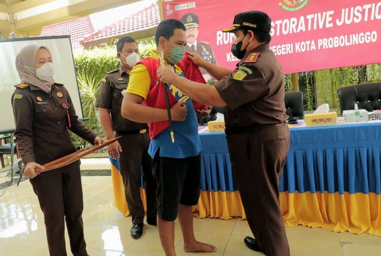 Kajari Kota Probolinggo, Hartono (kanan) membantu melepas rompi tahanan yang dikenakan Tomy Angga Kusuma. (Foto: Ikhsan Mahmudi/Ngopibareng.id)