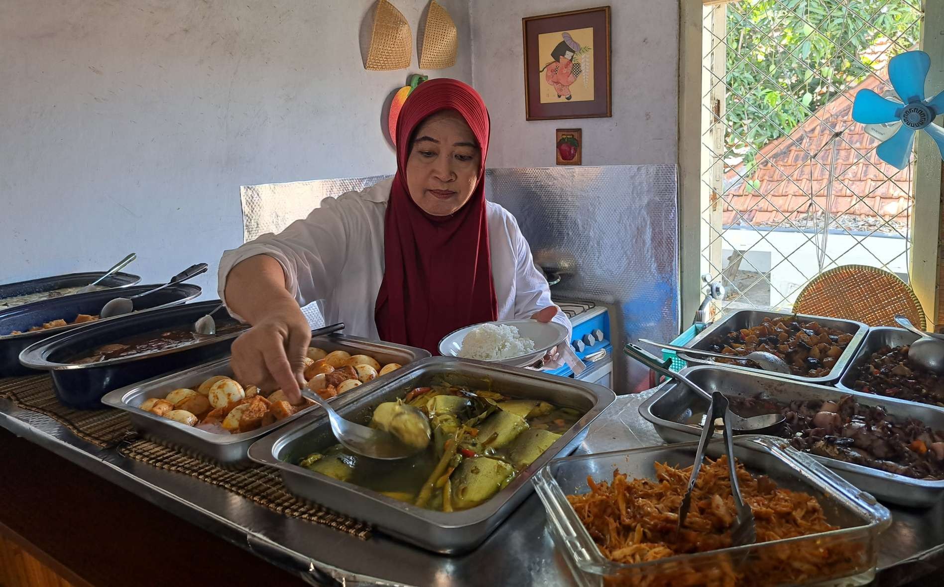 Eni Wisnu Wardhani melayani pelanggan yang ingin makan di warung di rumahnya.  (Foto: Pita Sari/Ngopibareng.id)