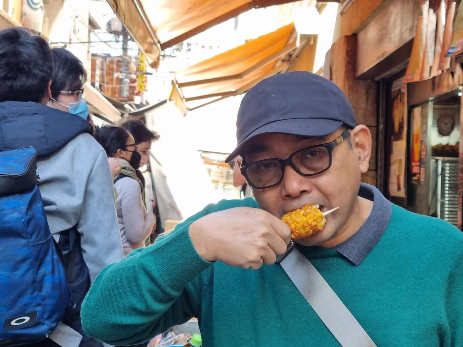 Arif Afandi makan dadar jagung, saat berkunjung ke Pasar Ikan Tsukiji. Inilah pasar legendaris yang ada di tengah kota Tokyo. Tak jauh dari pusat perbelanjaan paling hipe di Tokyo: Ginza. (Foto: wilis arif afandi/Ngopibareng.id)