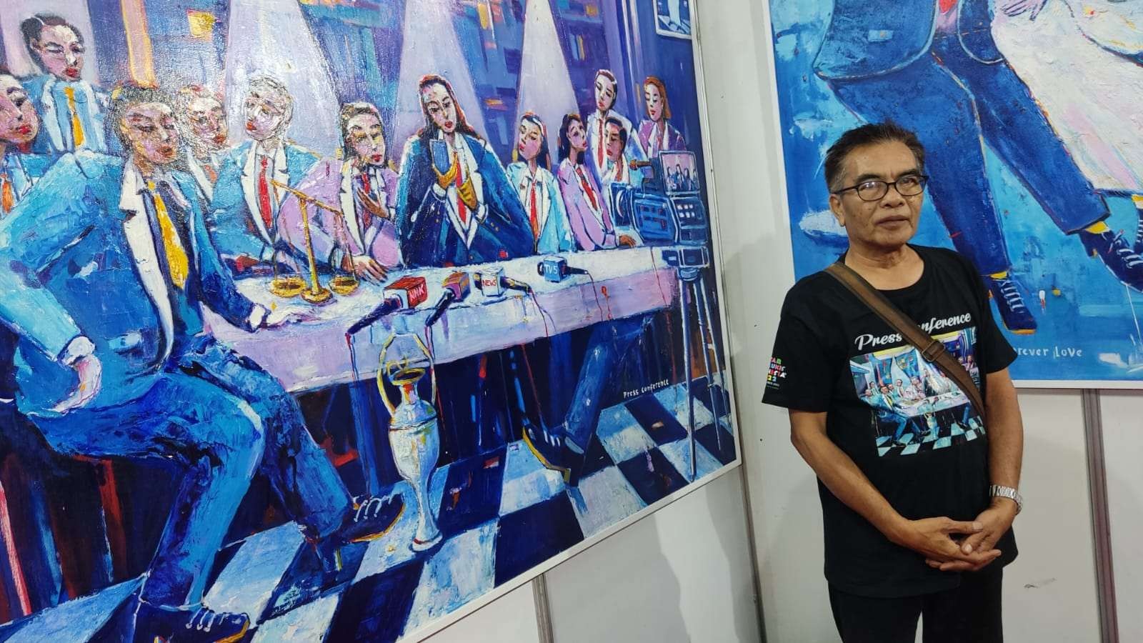 Pelukis, Djoko Sutrisno bersama karyanya berjudul Press Conference di arena PSLI 2022 Jatim Expo, Surabaya. (Foto: Fariz Yarbo/Ngopibareng.id)