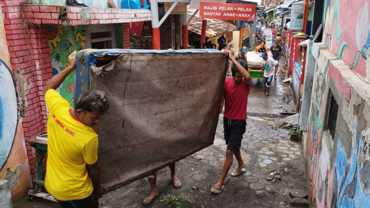 Warga Kelurahan Tukangkayu mengangkat kasur yang rusak akibat terendam banjir pada Senin malam. (Foto: Muh Hujaini/Ngopibareng.id)