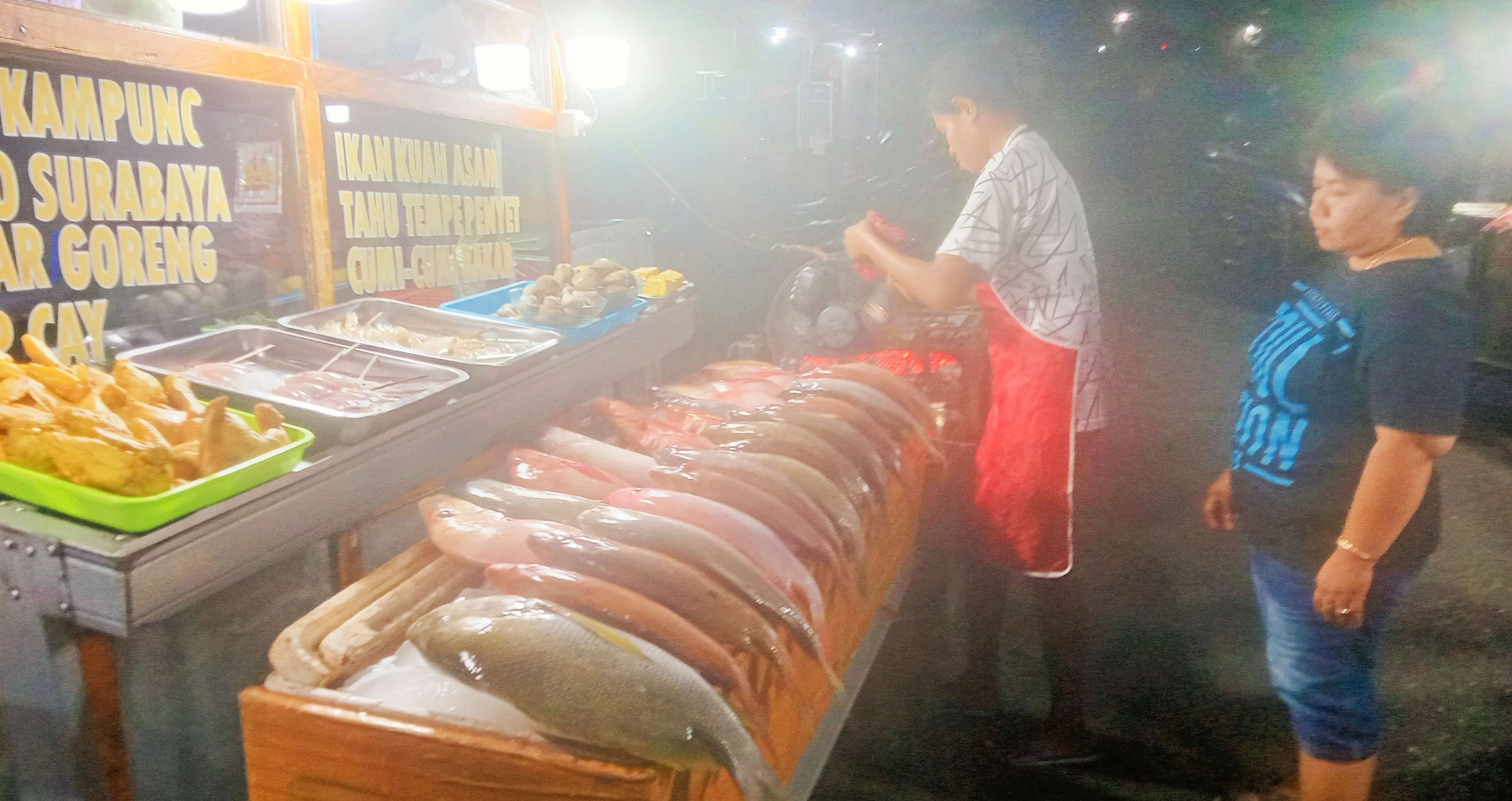 Neng Ninik memanjakan penggemar ikan bakar di Pasar Malam Solor Kupang, dengan sambal khas Surabaya. Nikmatnya pol. (Foto: Asmanu Sudharso/Ngopibareng.id)