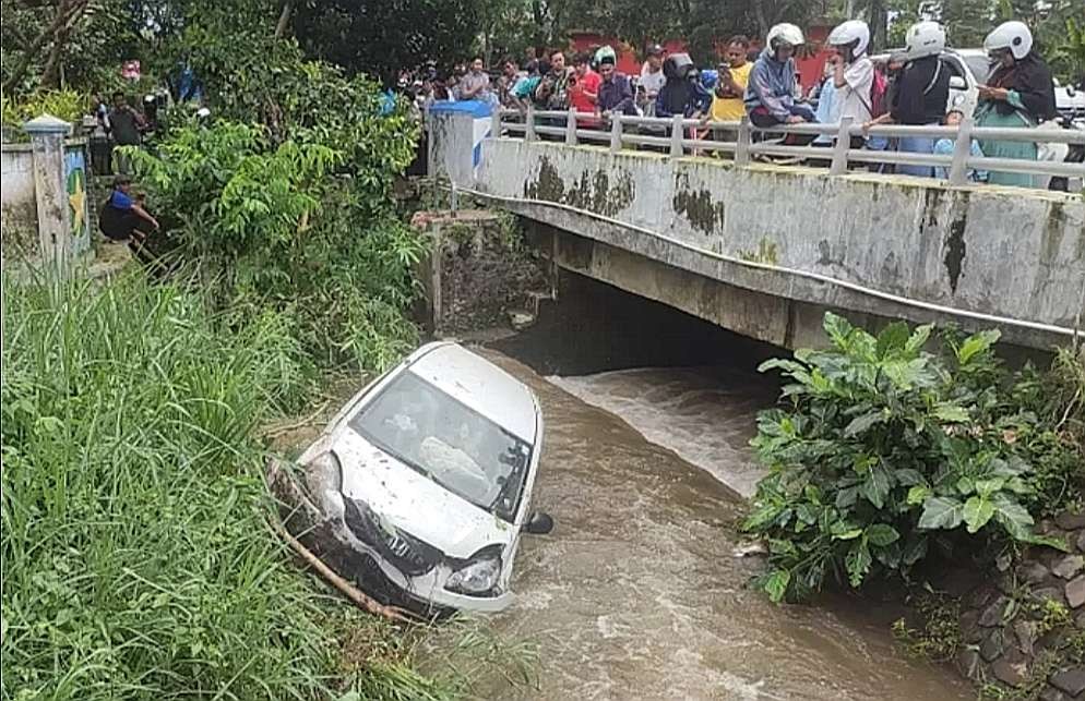 Mobil Honda Brio tercebur ke sungai di Bondowoso jadi tontonan warga. (Foto: istimewa/Ngopibareng.id)