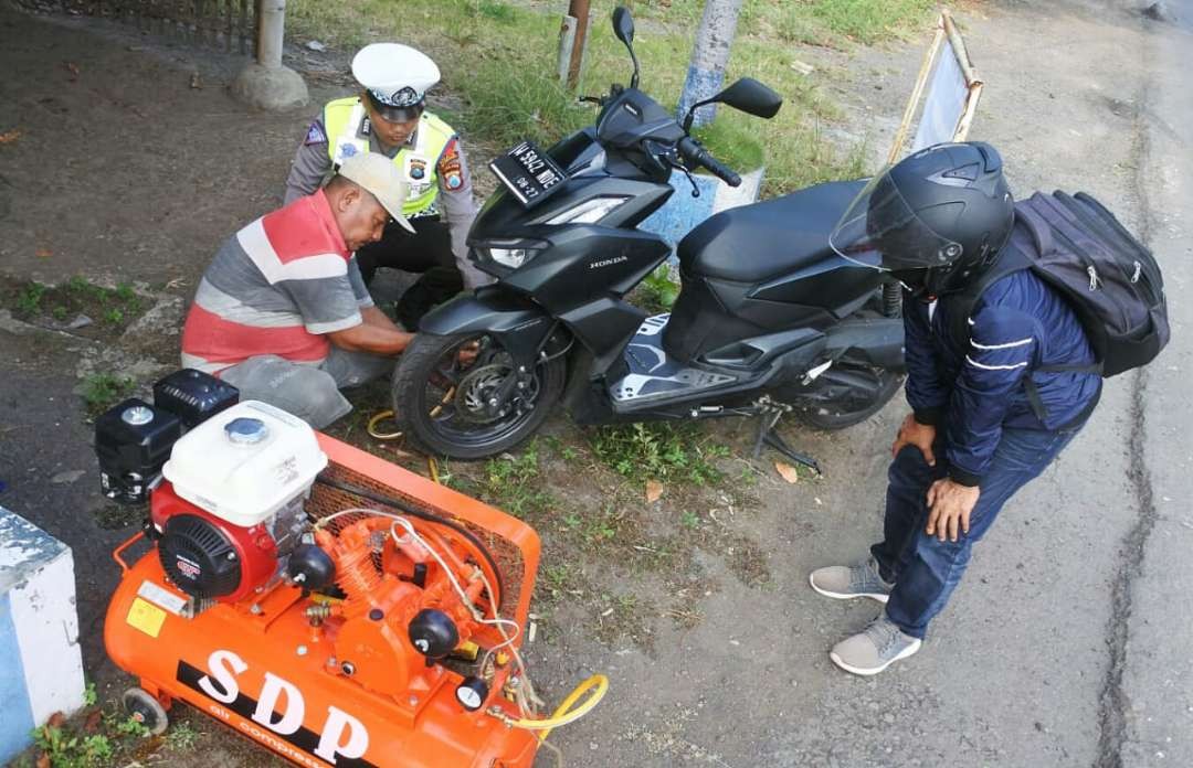 Polisi mengawal petugas tambal ban menambal gratis ban bocor sepeda motor pemudik Idul Fitri 2023 melewati Jalur Pantura Situbondo.(Foto: Guido/Ngopibareng.id)