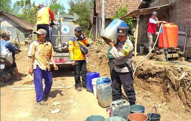 Petugas BPBD Situbondo dibantu anggota Bhabinkamtibmas Polsek Arjasa membagikan air bersih di dusun kekurangan air bersih. (Foto: Guido Saphan/Ngopibareng.id)