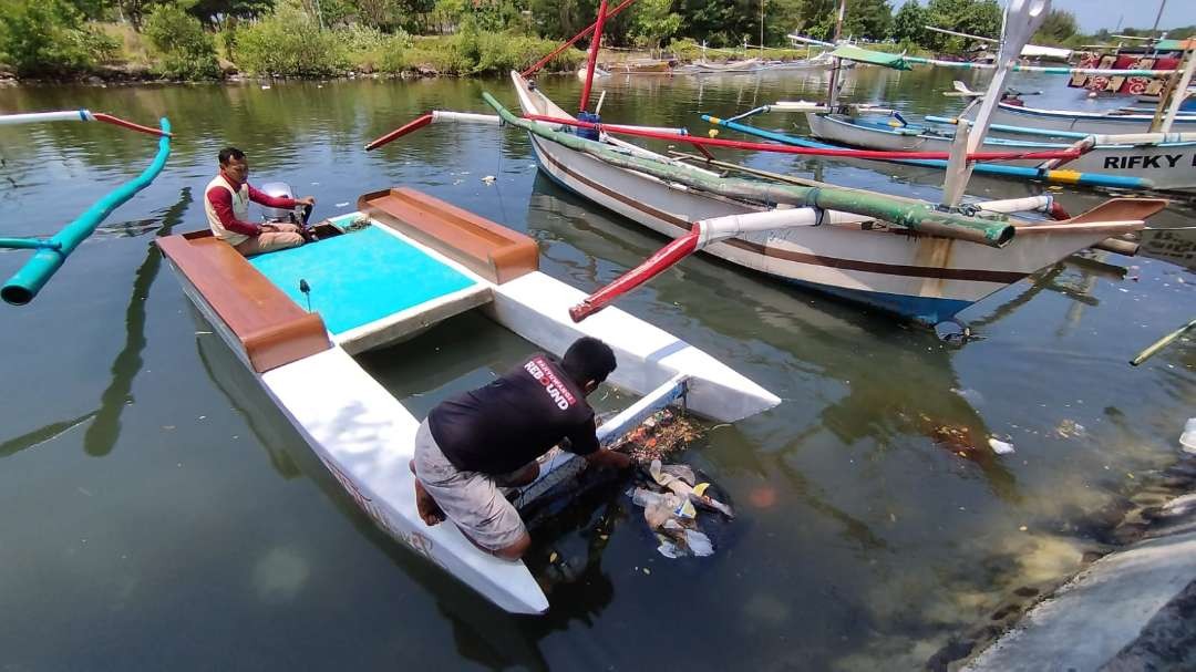 Anggota Pokdarwis Kampung Mandar membersihkan sampah di muara dengan menggunakan perahu sampah yang dibuat sendiri (foto: Muh Hujaini/Ngopibareng.id)