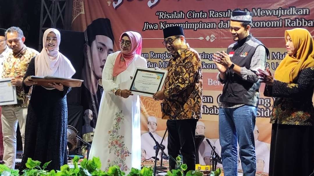 Ketua DMI Surabaya, Arif Affandi, menerima penghargaan dari FEB Unesa yang disampaikan Wadek II Dr Susanti dalam kegiatan Pengajian Akbar dan Gebyar Sholawat di Halaman Gedung G2-G3 FEB Unesa, Surabaya, Senin 2 Oktober 2023.  (Foto: Fariz Yarbo/Ngopibareng.id)