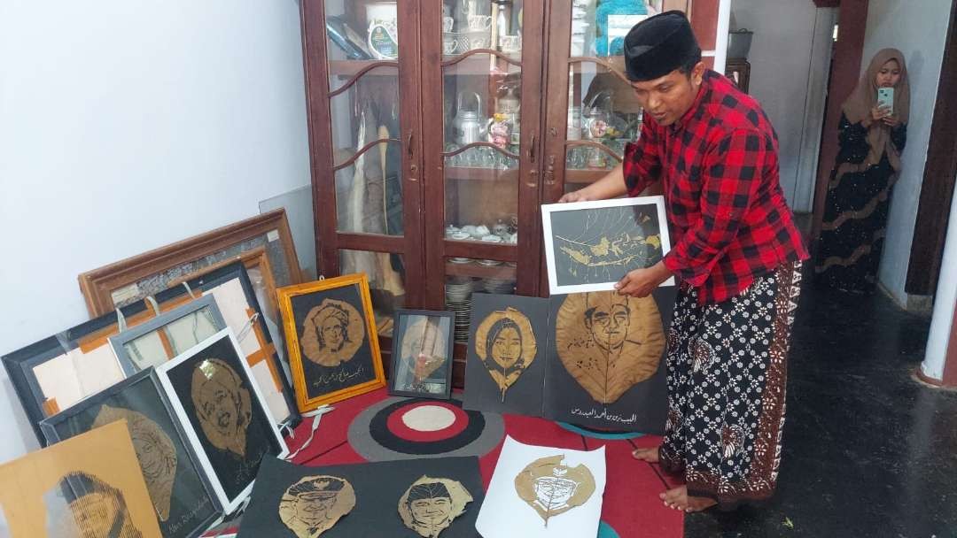 Rijarullah menunjukkan karyanya, lukisan ukir pada selembar daun jati kering di rumahnya, Desa Wringinanom, Kecamatan Kuripan, Kabupaten Probolinggo. (Foto: Ikhsan Mahmudi/Ngopibareng.id)