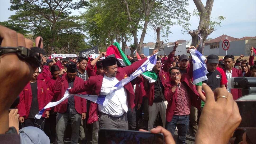 Seorang pengunjuk rasa dari Ikatan Mahasiswa Muhammadiyah merobek bendera Israel di Kantor Konjen AS di Jalan Citra Raya Niaga, Surabaya,  pada Selasa 7 November 2023. (Foto: Julianus Palermo/Ngopibareng.id)