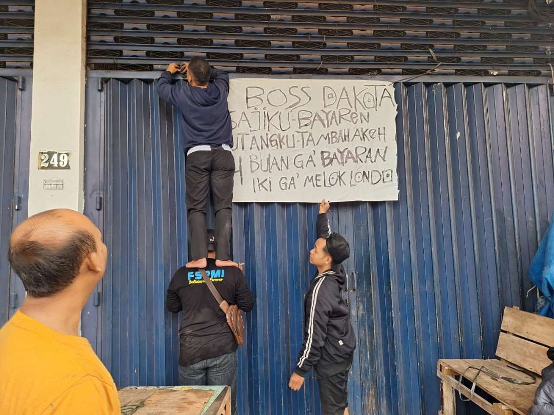 Para pengunjuk rasa memasang poster protes di depan kantor Dakota, Jalan Demak, Dupak, Krembangan, Surabaya. (Foto: Julianus Palermo/Ngopibareng.id)