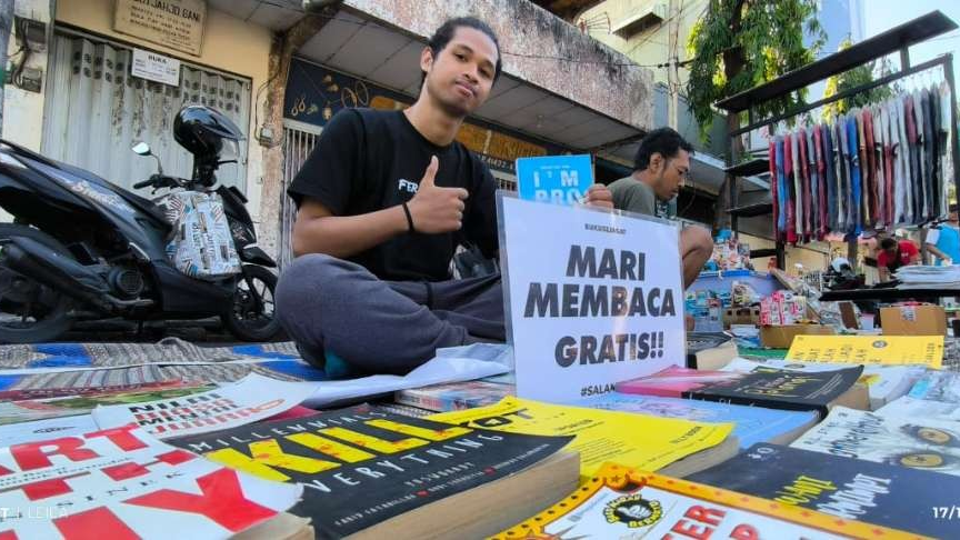 Sebastian Yudi mengajak para pengunjung untuk membaca puluhan buku koleksinya secara gratis. (Foto: Fendi Lesmana/Ngopibareng.id)