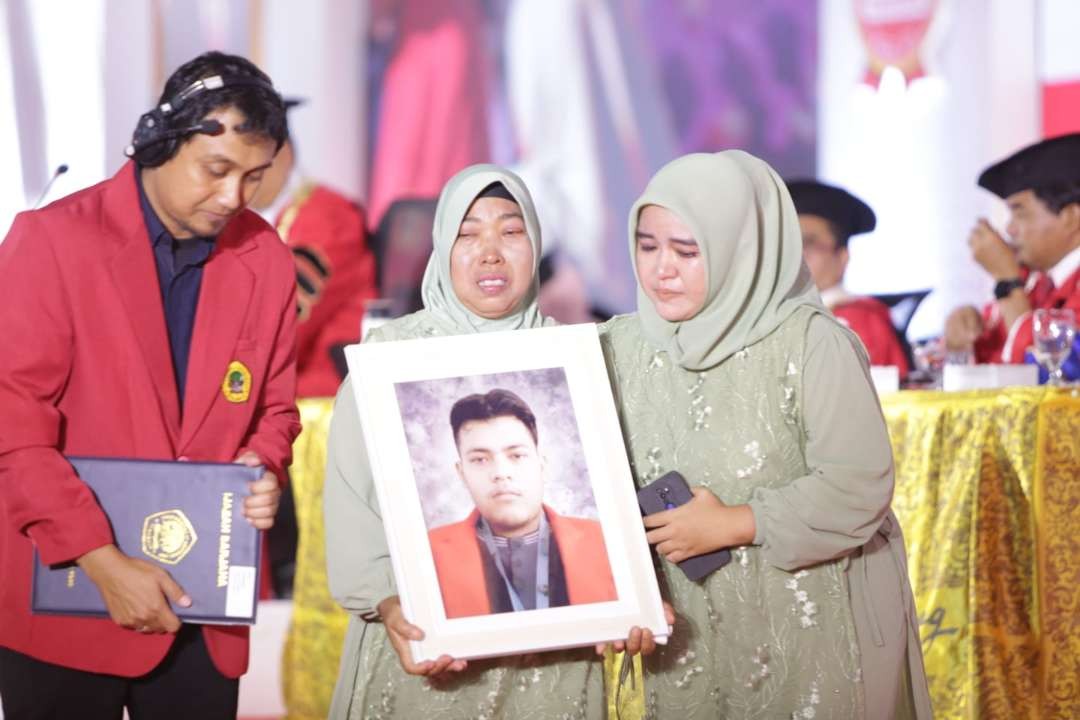 Rendy mahasiswa Untag Surabaya meninggal sebelum wisuda digantikan sang ibu sambil membawa foto sang anak. (Foto: Dokumentasi Untag)